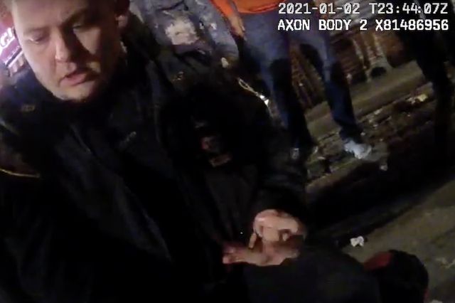 A screenshot of bodycam footage of Officer Thomas Montario putting handcuffs on Sircarlyle Arnold, who is lying down and facing away from the camera.